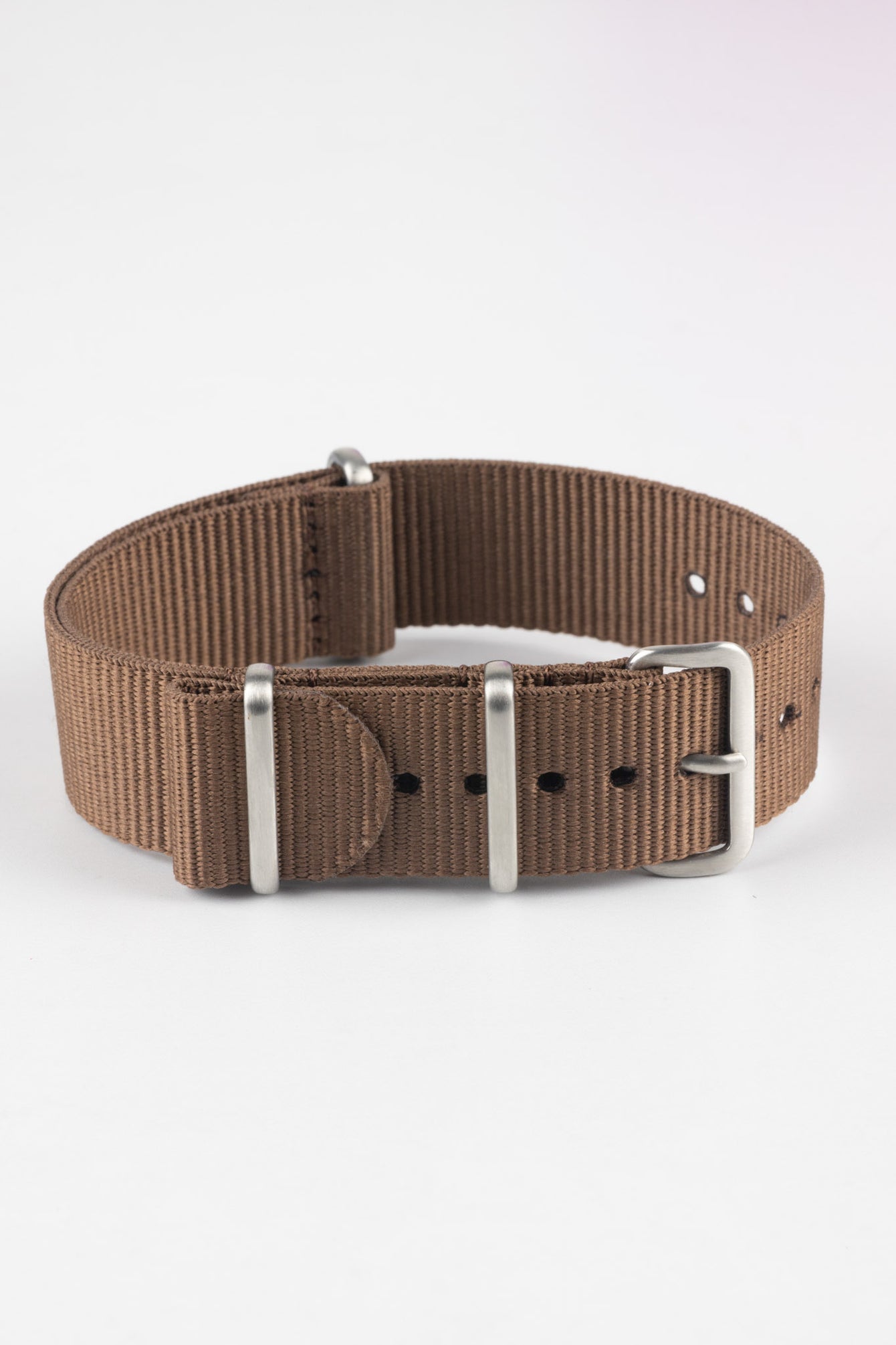 Close-up product shot of a brown ribbed nylon NATO‑style watch strap with brushed metal buckle and keepers, arranged in a loop on a plain light background, highlighting its woven texture and adjustment holes.