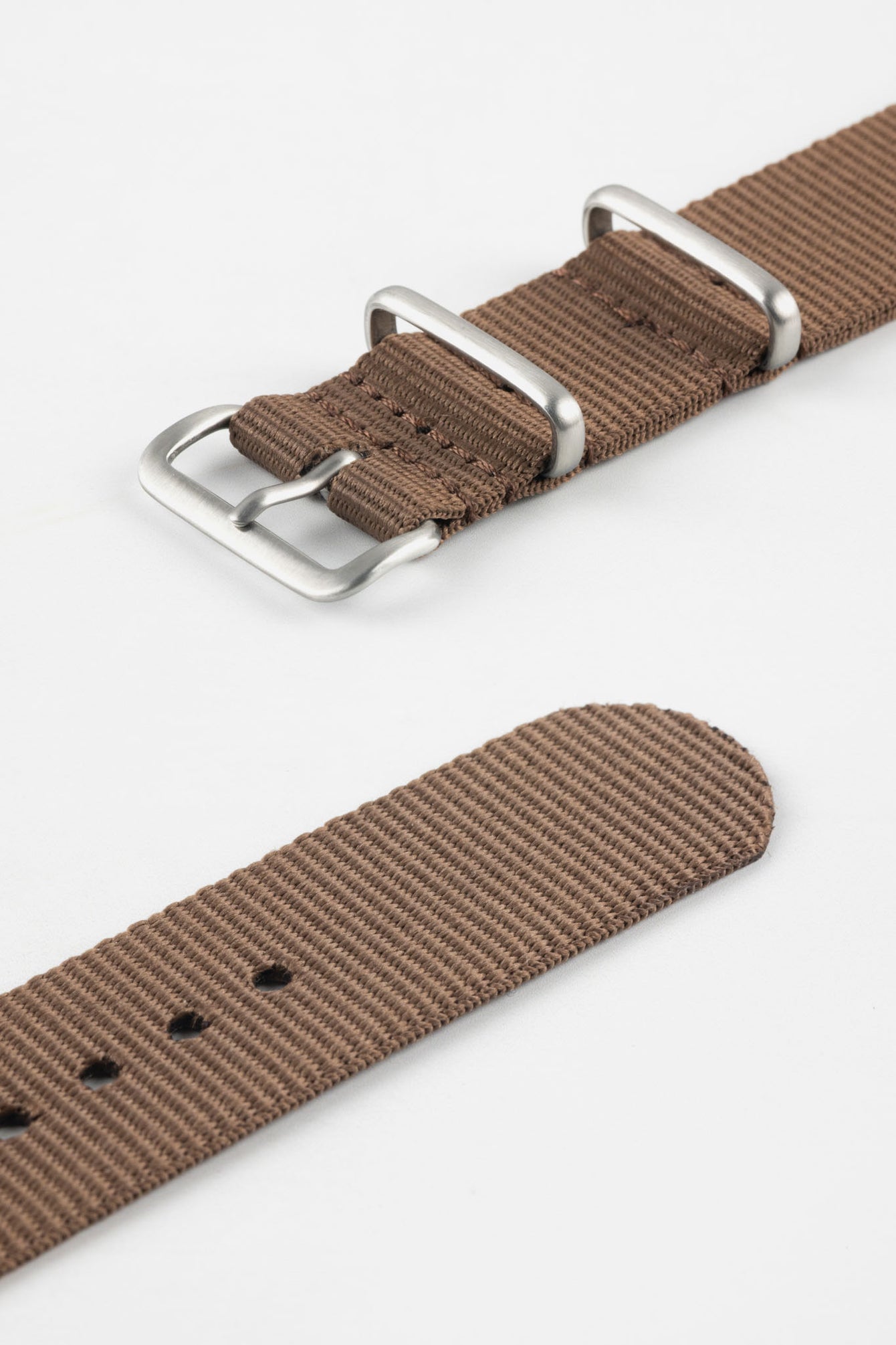 Close-up product shot of a brown ribbed nylon NATO‑style watch strap, showing brushed metal buckle, keepers, stitching, and adjustment holes, isolated against a plain light background.