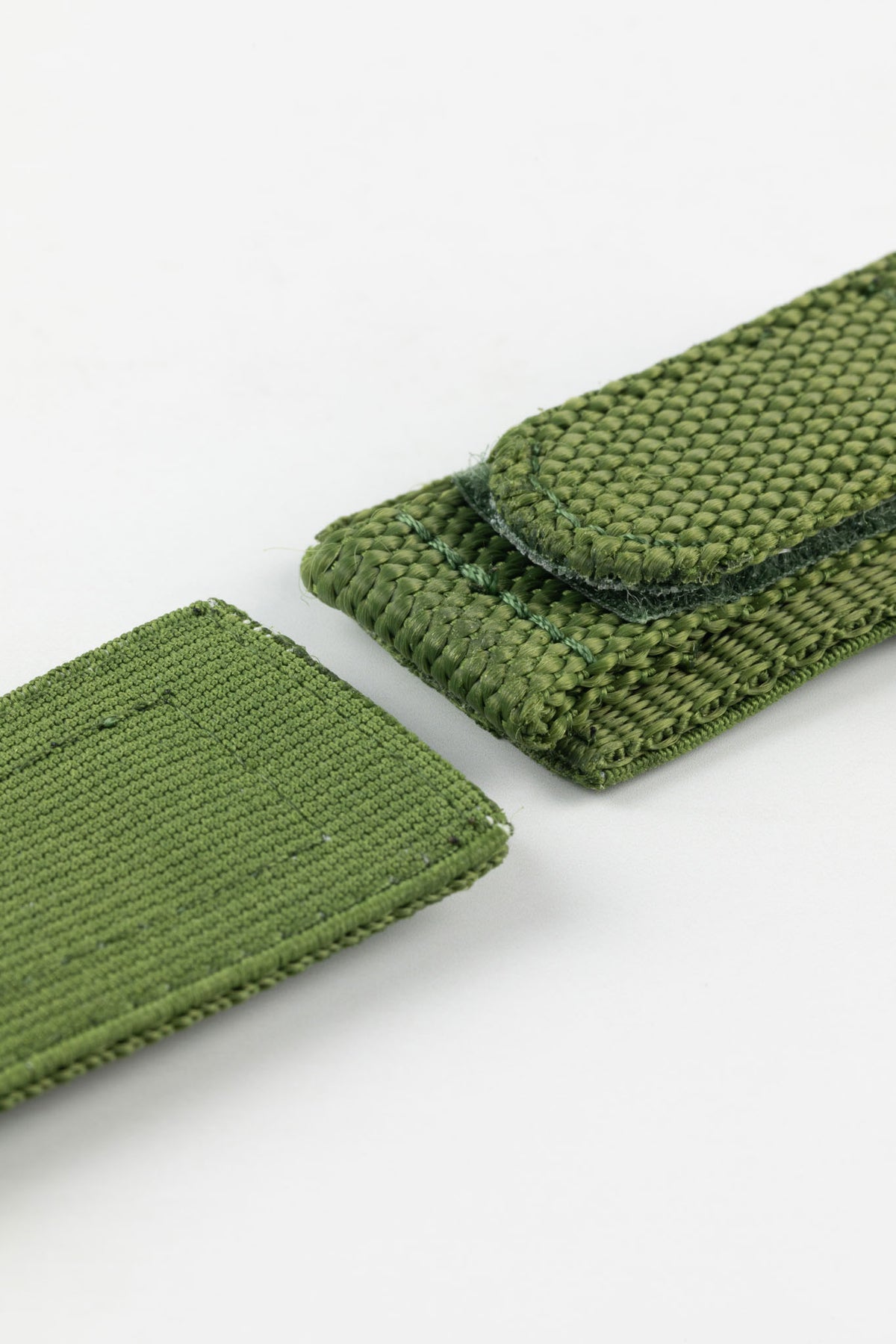 Close-up of an olive green tactical hook-and-loop watch strap displayed partially opened against a clean white background.