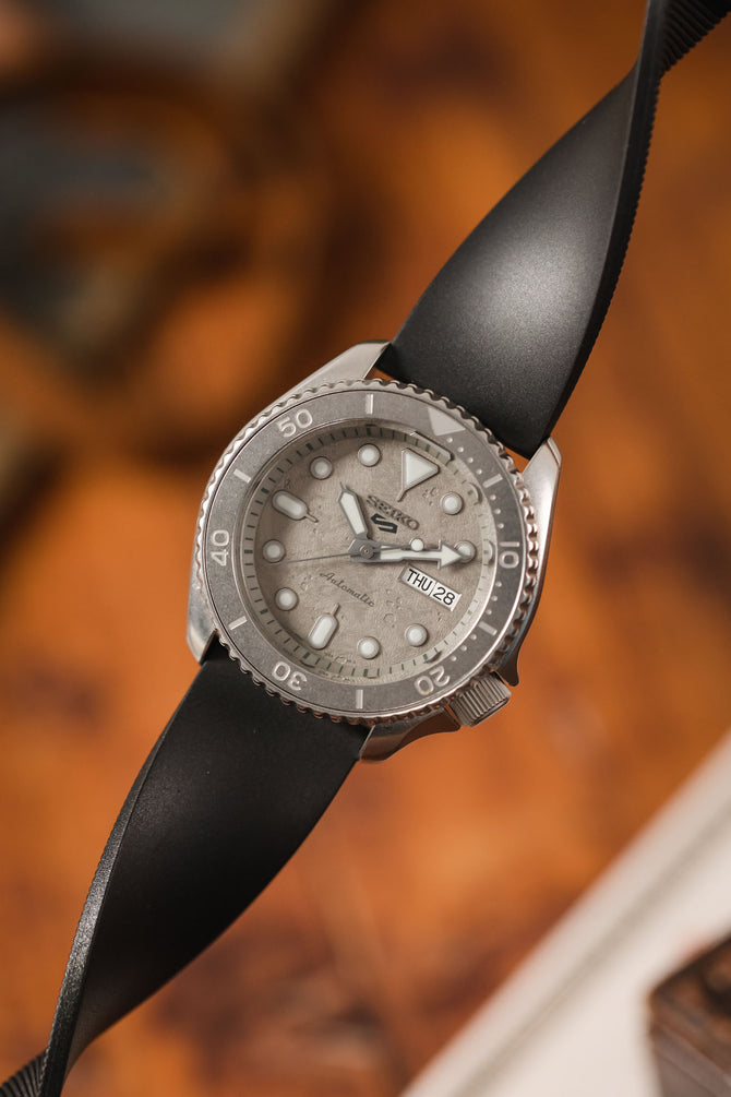 Seiko 5 Sports Cement SRPG61K1 with Black Bonetto Cinturini 270 twisted to show flexibility and durability