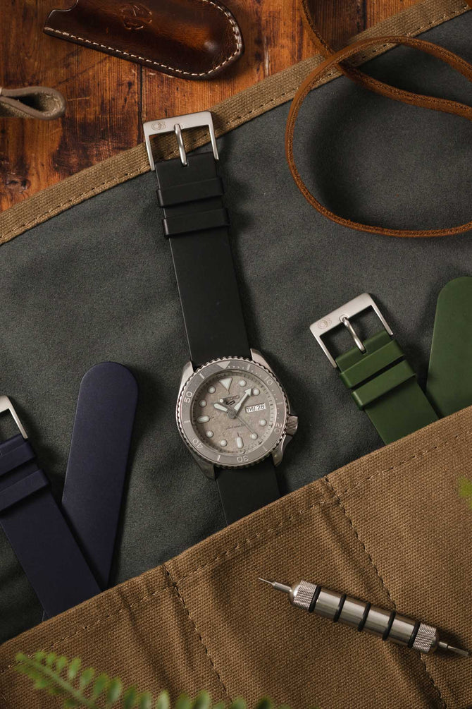 Seiko 5 Sports Cement SRPG61K1 with Black Bonetto Cinturini 270 Rubber wach strap flat on wooden table in watch kit