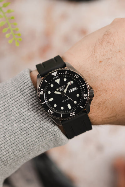 Seiko 5 sports SRPD65K1 gunmetal with black bonetto cinturini 319 rubber watch strap on wrist with grey jumper