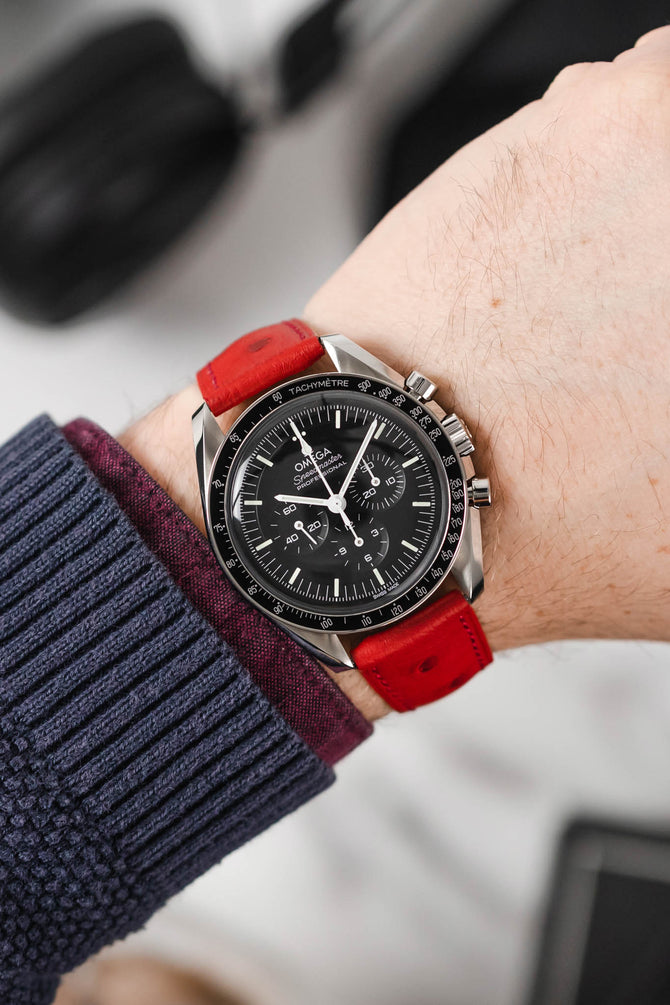 Black Omega Moonwatch Speedmaster fitted with Hirsch Massai Ostrich red leather watch strap worn on wrist