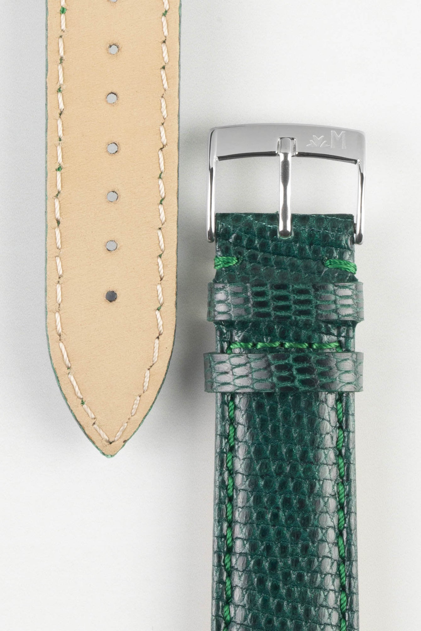 A top-down, close-up shot of a two-piece dark green watch strap with a lizard-skin texture, laid vertically on a white surface. The right piece shows the green exterior with a silver-toned buckle and prominent green stitching. The left piece shows the light brown leather underside with a series of circular holes for adjustment and visible green stitching along its edge.